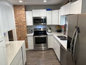 Kitchen featuring stainless steel appliances, dark wood-type flooring, recessed lighting, light countertops, and decorative backsplash