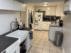 Kitchen with white appliances, dark countertops, backsplash, and white cabinetry