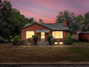 View of front of house featuring brick siding, a lawn, a chimney, and roof with shingles