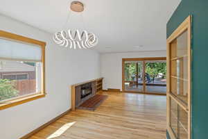 Unfurnished living room with light wood-type flooring, healthy amount of natural light, a chandelier, and a brick fireplace