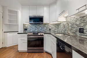 Kitchen featuring appliances with stainless steel finishes, backsplash, white cabinets, and wood finished floors