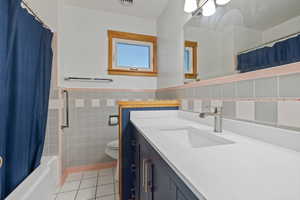 Bathroom with tile patterned floors, vanity, tile walls, shower / tub combo, and a wainscoted wall