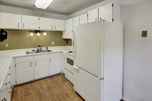 Kitchen with white appliances, light wood-style floors, white cabinetry, and light countertops