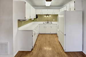 Kitchen featuring freestanding refrigerator, light wood finished floors, light countertops, and white cabinetry