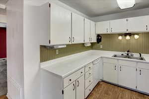 Kitchen featuring white cabinetry, wood finished floors, light countertops, and dishwasher