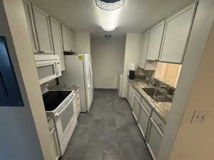 Kitchen featuring white appliances, white cabinets, and stone counters
