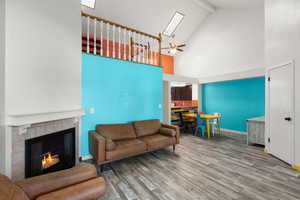 Living area featuring wood finished floors, a tile fireplace, ceiling fan, beam ceiling, and high vaulted ceiling