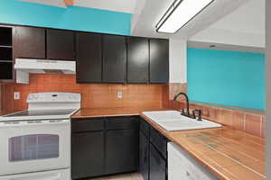Kitchen with white appliances, under cabinet range hood, tile countertops, and tasteful backsplash
