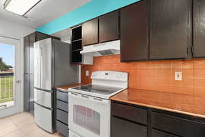 Kitchen with under cabinet range hood, electric stove, tile countertops, and freestanding refrigerator