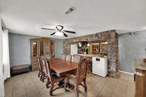 Dining space with light tile patterned floors, a ceiling fan, and a textured ceiling.