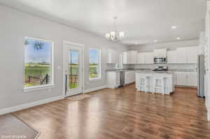 Kitchen featuring appliances with stainless steel finishes, a chandelier, recessed lighting, white cabinets, and a kitchen bar