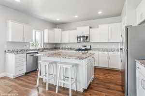 Kitchen with stainless steel appliances, a center island, white cabinets, a kitchen breakfast bar, and recessed lighting