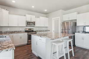 Kitchen with appliances with stainless steel finishes, a kitchen island, dark wood-style floors, a kitchen bar, and light stone counters
