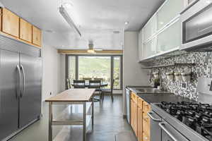 Kitchen with stainless steel appliances, finished concrete flooring, decorative backsplash, ceiling fan, and dark countertops