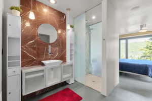 Ensuite bathroom featuring finished concrete floors, a walk in shower, vanity, tile walls, and recessed lighting