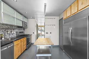Kitchen with stainless steel appliances, concrete flooring, backsplash, recessed lighting, and glass insert cabinets