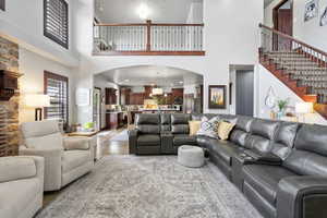 Living area featuring a towering ceiling, light wood finished floors, stairway, and arched walkways