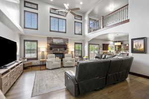 Living area featuring a ceiling fan, a towering ceiling, a fireplace, and wood finished floors