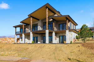 Rear view of house with stone siding, a patio, and a balcony