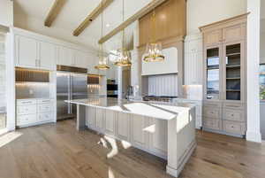 Kitchen featuring high vaulted ceiling, decorative light fixtures, stainless steel appliances, a kitchen island with sink, and light wood-style flooring