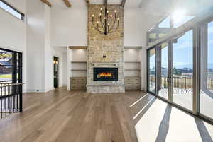 Unfurnished living room featuring wood finished floors, a towering ceiling, a fireplace, built in shelves, and a chandelier