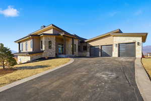 View of front facade featuring stone siding, driveway, and a garage