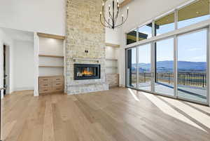 Unfurnished living room featuring light wood-style floors, a mountain view, a towering ceiling, built in shelves, and a fireplace