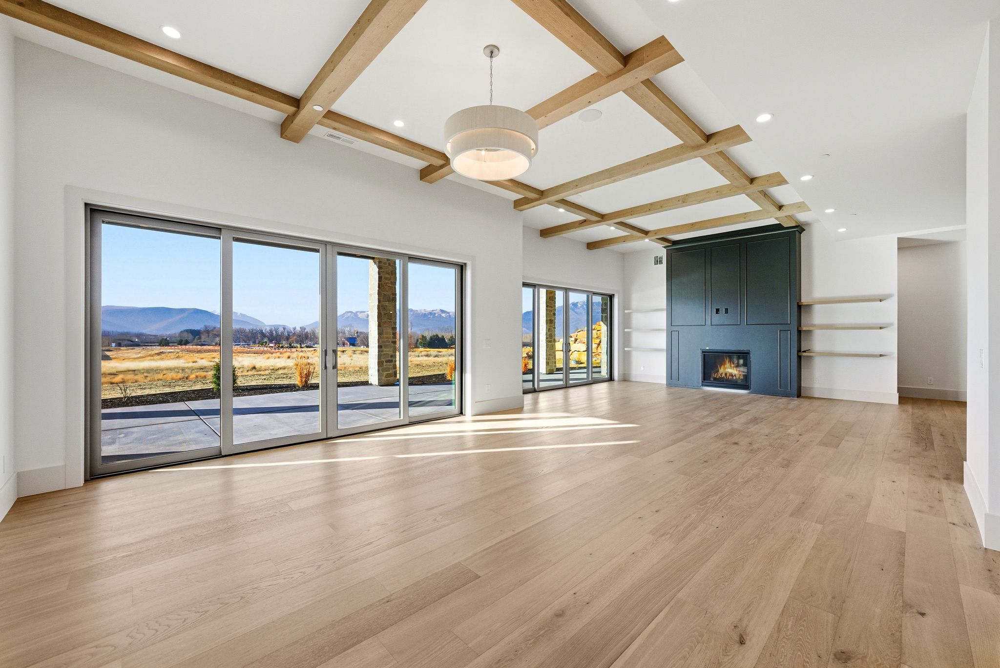 Unfurnished living room with coffered ceiling, beam ceiling, a mountain view, light wood finished floors, and a fireplace