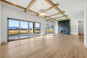 Unfurnished living room with coffered ceiling, beam ceiling, a mountain view, light wood finished floors, and a fireplace