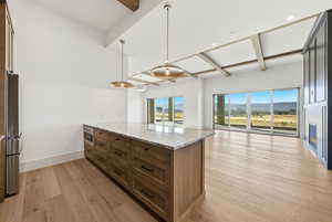Kitchen with light stone countertops, hanging light fixtures, a peninsula, open floor plan, and beamed ceiling