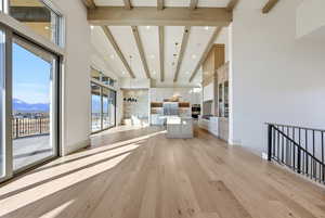 Unfurnished living room featuring light wood-type flooring, a mountain view, beam ceiling, and a towering ceiling