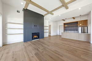 Unfurnished living room with recessed lighting, a large fireplace, light wood finished floors, and beam ceiling