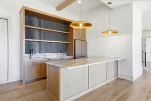 Kitchen with light stone counters, pendant lighting, a peninsula, open shelves, and freestanding refrigerator
