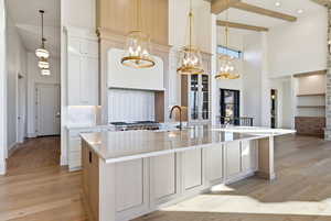 Kitchen featuring a towering ceiling, light stone counters, decorative light fixtures, a center island with sink, and light wood-style flooring
