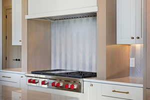 Kitchen with white cabinetry, premium range hood, stainless steel gas cooktop, and light stone counters