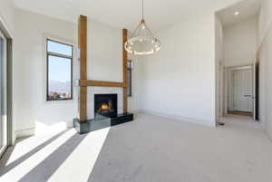 Unfurnished living room with a high ceiling, a chandelier, a fireplace, and carpet floors