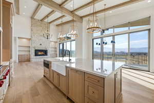 Kitchen featuring a fireplace, light wood finished floors, hanging light fixtures, light stone countertops, and a large island with sink