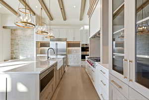Kitchen featuring pendant lighting, a chandelier, white cabinets, tasteful backsplash, and beamed ceiling