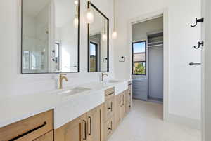Full bath with double vanity, a stall shower, a spacious closet, and light flooring