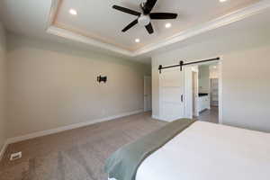 Bedroom featuring a barn door, recessed lighting, a raised ceiling, light colored carpet, and a spacious closet