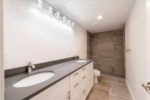 Bathroom featuring a tile shower, double vanity, and recessed lighting