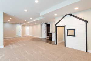 Unfurnished living room featuring a barn door, light carpet, recessed lighting, and beverage cooler