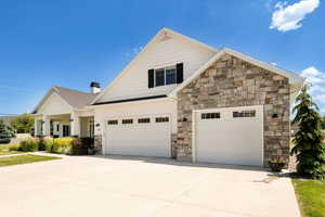 View of front of property with driveway, stone siding, a chimney, and an attached garage