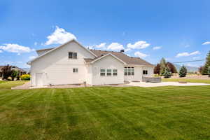 Back of house featuring a hot tub, a lawn, and a patio