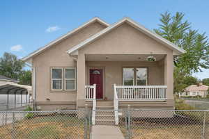 View of front of property with covered porch, a gate, stucco siding, a carport, and a fenced front yard