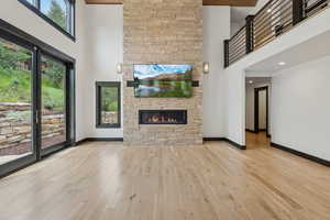 Unfurnished living room with a high ceiling, a stone fireplace, and wood finished floors