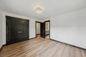 Unfurnished bedroom featuring light wood-style floors, a chandelier, a closet, and connected bathroom