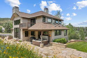 Rear view of property with a chimney, a balcony, a patio area, a shingled roof, and a hot tub