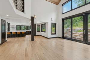 Unfurnished living room with high vaulted ceiling, light wood-style flooring, and healthy amount of natural light