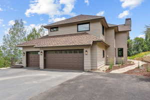 View of front of home with a chimney, asphalt driveway, an attached garage, and a shingled roof